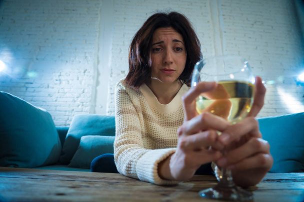 Portrait of depressed woman drinking glass of wine alone at home. Feeling distress, hopeless and frustrated, trying to feel better drinking. Unhealthy behavior, depression and alcohol concept. - Foto, imagen