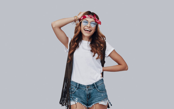 laughing stylish young woman in red bandanna on head standing against grey background - Fotoğraf, Görsel