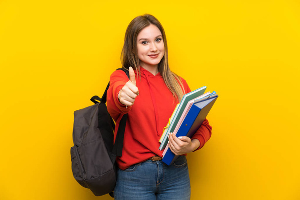 Genç öğrenci kız üzerinde sarı arka plan veren bir thumbs yukarı jest - Fotoğraf, Görsel