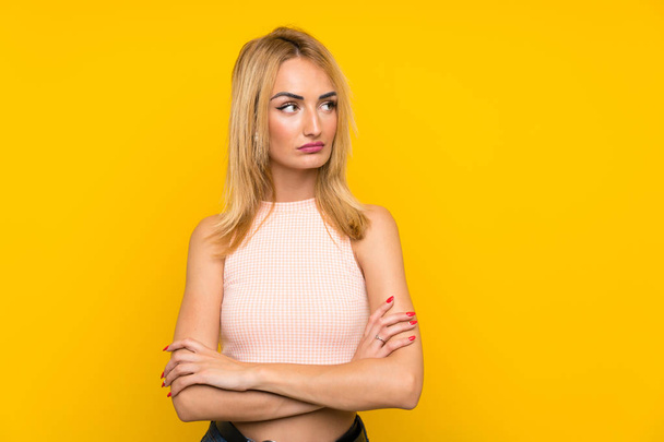 Young blonde woman over isolated yellow wall looking side - Foto, Imagem