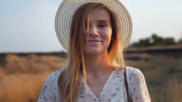 Romantic and carefree young woman in wicker hat in slow motion video walking on field enjoying freedom and calmness on rural nature during vacations holidays. Close up portrait.  - Кадри, відео