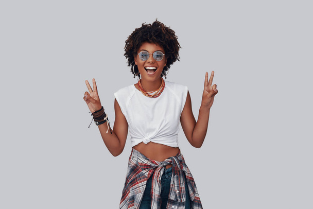 smiling young African woman looking at camera and posing in studio, gesturing peace with fingers  - Photo, Image