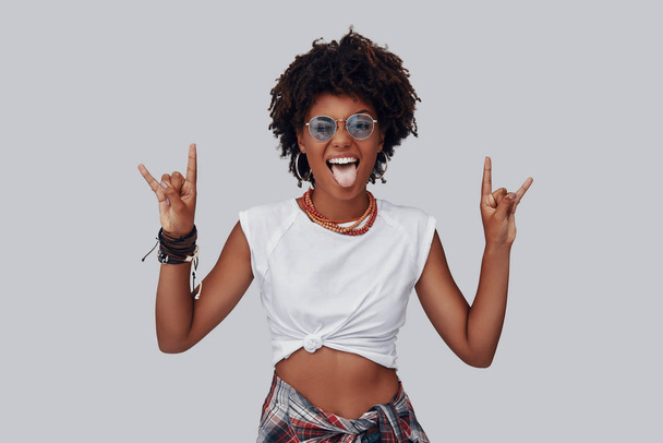 funny young African woman looking at camera and gesturing punk rock with hands  - Fotó, kép