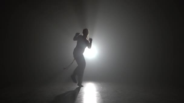 Frau mit langen Haaren übt Capoeira im Dunkeln gegen Scheinwerferlicht im Studio. - Filmmaterial, Video