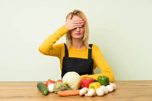 Young blonde woman with lots of vegetables covering eyes by hands - Photo, Image