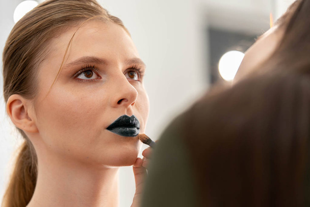 Makeup artist applies blue lipstick. Hand of make-up master, painting model lips - Φωτογραφία, εικόνα