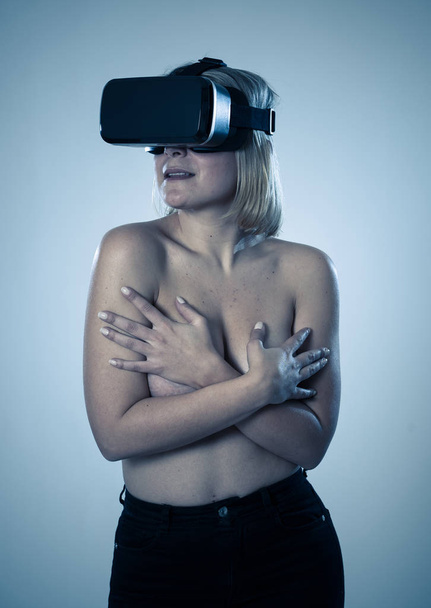 Sensual attractive woman using augmented or virtual reality goggles feeling excited exploring virtual sexuality while getting topless covering her breast. In cyber sex VR simulator and new technology. - Foto, imagen