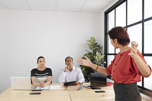 Деловой тренер, проводящий бизнес-тренинг для деловых людей, она стоит и объясняет что-то, слушая ее в офисе
 - Фото, изображение
