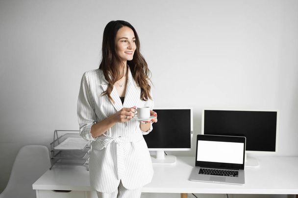 das Mädchen trinkt eine Tasse Kaffee in einem hellen Büro - Foto, Bild