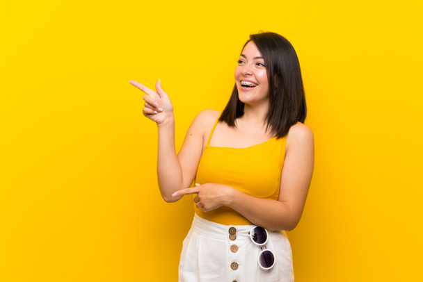 Jeune femme mexicaine sur fond jaune isolé pointant du doigt sur le côté
 - Photo, image