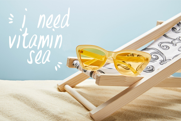 Žluté elegantní sluneční brýle na palubě židle na písku a modrém pozadí potřebuji - Fotografie, Obrázek