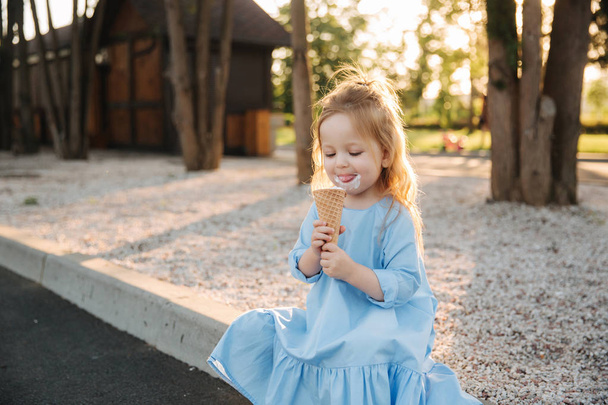schönes kleines Mädchen in einem blauen Kleid, das ein Eis isst - Foto, Bild