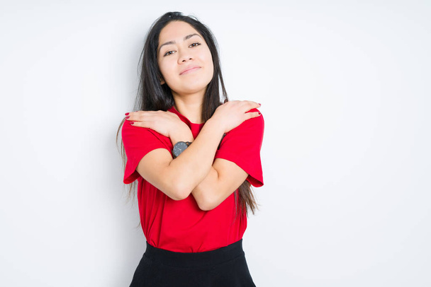 Beautiful brunette woman wearing red t-shirt over isolated background Hugging oneself happy and positive, smiling confident. Self love and self care - Photo, Image