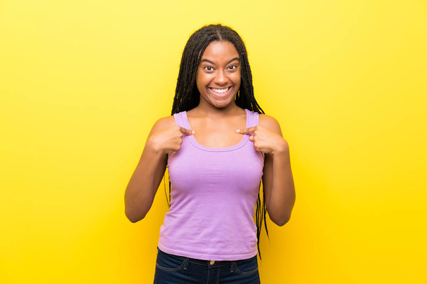 驚きの表情で孤立した黄色の壁の上に長い編組髪を持つアフリカ系アメリカ人のティーンエイジャーの女の子 - 写真・画像