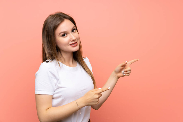 Teenager Mädchen über isolierte rosa Wand zeigt mit dem Finger zur Seite - Foto, Bild