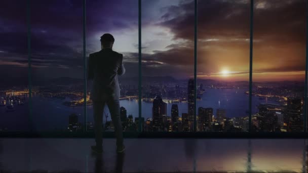 Silhouet van de zakenman in het kantoor staande voor een groot raam met uitzicht op Hong Kong. Praten over een telefoon en het bespreken van zaken - Video