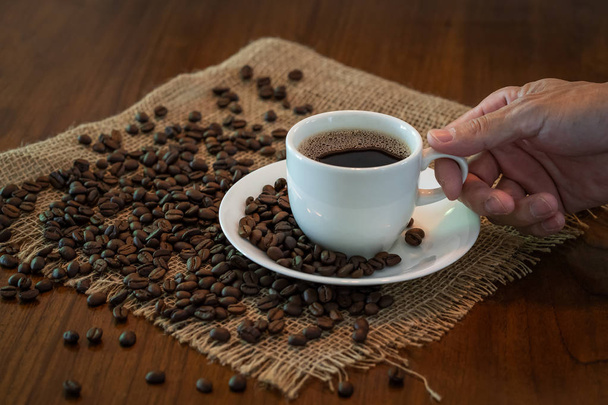 Чашка горячего кофе с жареными кофейными зернами на деревянном столе
 - Фото, изображение