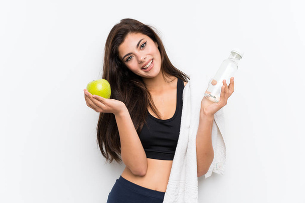 Teenager sport girl over isolated white background with an apple and a bottle of water - Foto, imagen
