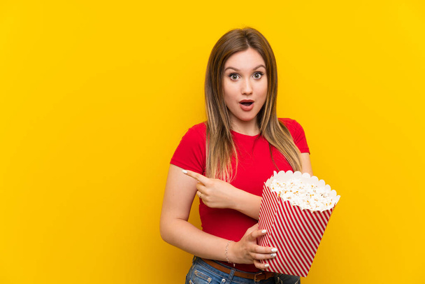 Young woman with popcorns over pink wall surprised and pointing side - Фото, зображення