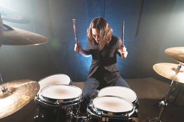 Portrait of a long-haired drummer with chopsticks in his hands sitting behind a drum set. Low key. Concepts of the creative freedom of the millenial generation - Φωτογραφία, εικόνα