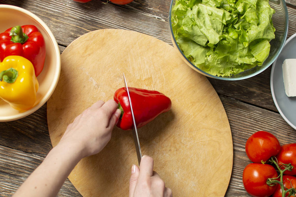 Hände eines Mädchens schneiden Paprika auf einem Holztisch, der Prozess der Herstellung von vegetarischem Salat, Nahaufnahme Schneiden von Gemüse - Foto, Bild