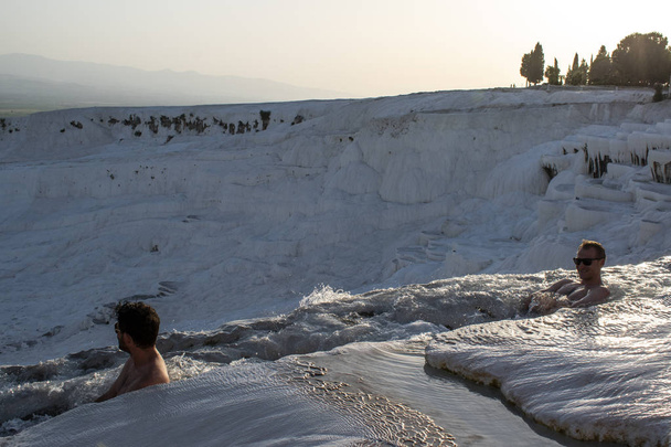 Türkiye, 07/10/2019: güneş batımında, Pamukkale 'de Traverten teraslarında (Cotton Castle), su tarafından yatırılan sedimanlı kayanın ünlü doğal alanı olan kaplıcalardan akan suyun tadını çıkaran erkekler - Fotoğraf, Görsel