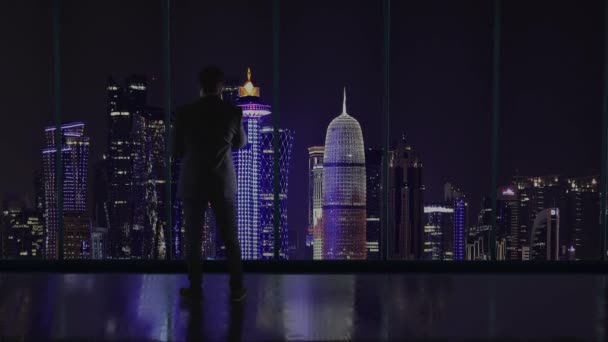 Silueta del hombre de negocios en la oficina de pie frente a una gran ventana con vistas a Doha, Quatar. Hablar por teléfono y hablar de negocios
 - Metraje, vídeo