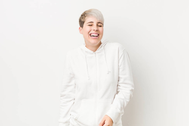 Young curvy woman wearing a white hoodie laughs and closes eyes, feels relaxed and happy. - Photo, image