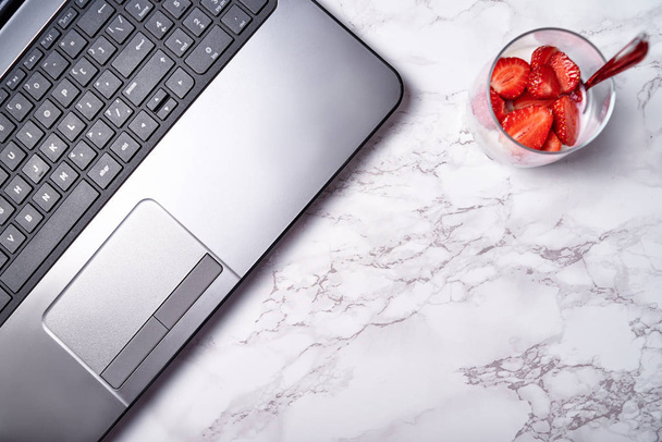 Glass of healthy yogurt with fresh sliced strawberry and laptop  - Foto, Bild