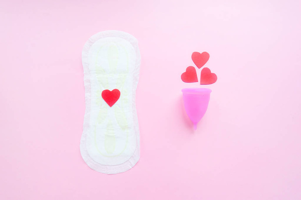 Herbruikbare menstruele beker met rode harten en menstruele pad op roze achtergrond, concept vrouwelijke intieme hygiëne periode producten en nul afval. Platte lay, minimalisme, Top uitzicht. copyspace - Foto, afbeelding