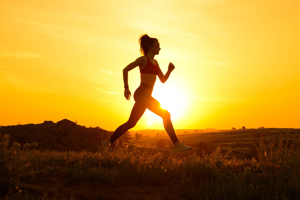 暑い夏の夕日の山道を走る若い美しい女性。スポーツとアクティブライフスタイル. - 写真・画像