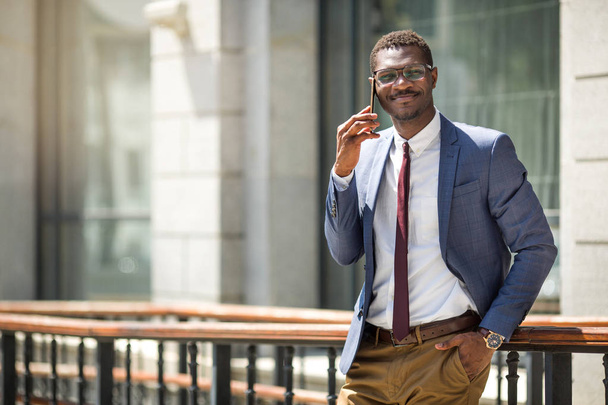 handsome young adult african man in suit and glasses talking on the phone - Valokuva, kuva