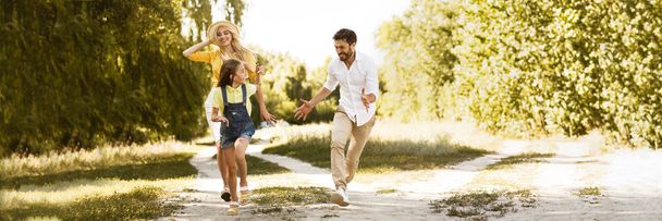 Happy girl running from her parents, having picnic in countryside - Φωτογραφία, εικόνα