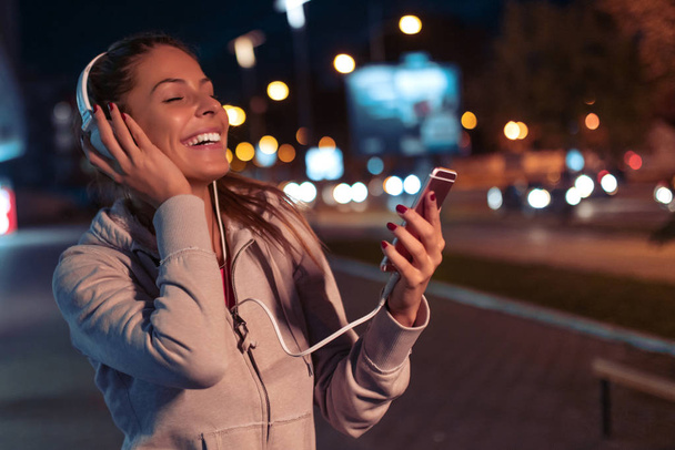 Jonge vrouw rent 's nachts in de stad en luistert naar muziek - Foto, afbeelding