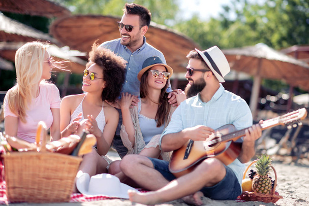 Happy friends relaxing and playing guitar on the beach. Having fun at beach party. - 写真・画像