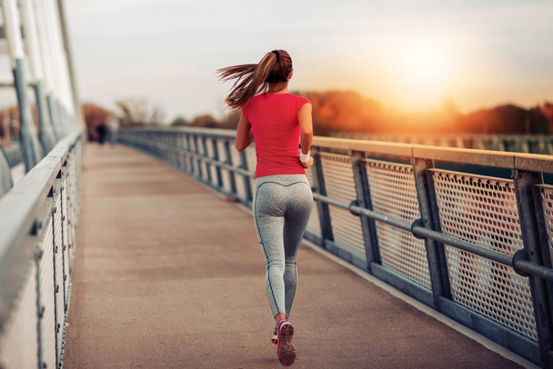 橋の上を走る若いフィットネス女性。スポーツ、フィットネス、健康、ライフスタイルの概念. - 写真・画像