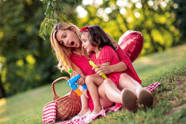 Beautiful mother and her daughter blowing soap bubbles in the park. - Zdjęcie, obraz
