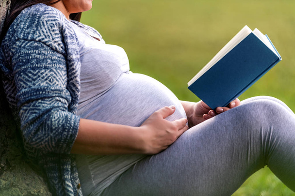 Terhes nő reaxing a parkban, és olvasás egy könyvet. - Fotó, kép