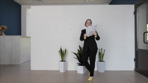pretty businesswoman dancing on high heels, throwing paper sheets against white wall and pot plants - Záběry, video