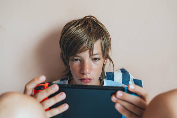Kid lying on couch and playing with a video game console at home - Photo, Image