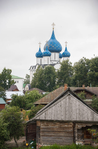 Een uitzicht op kleine dorp-grote kerk op een achtergrond-oud huis op een voorgrond-Suzdal, Rusland - Foto, afbeelding