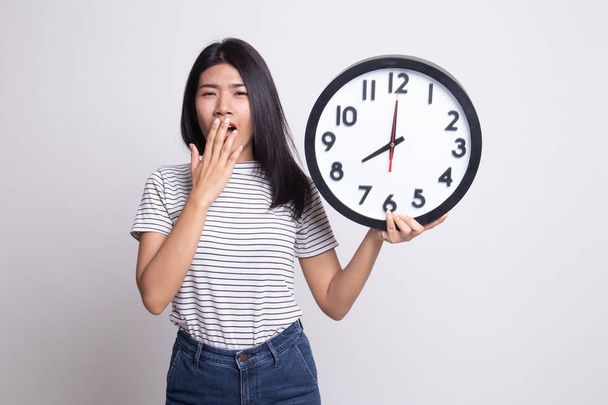 Sleepy young Asian woman with a clock in the morning. - Foto, Imagem