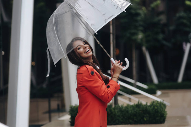 Außenporträt eines schönen jungen Mädchens, das lacht. junges Mädchen läuft mit Regenschirm auf der Straße. - Foto, Bild