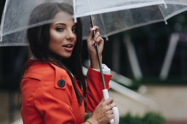 Close up woman portrait of young pretty girl posing at the city. Portrait of young woman in coat holding umbrella. Young smiling woman with umbrella on city street - Zdjęcie, obraz