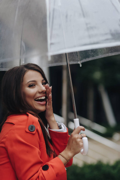 Pionowa kobieta portret młodego śmiać się ładna dziewczyna pozowanie w mieście. Portret młodej kobiety w płaszcz posiadający parasol - Zdjęcie, obraz