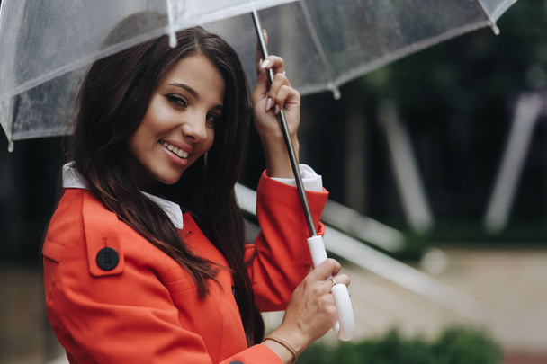 Bliska kobieta Portret młodej pięknej dziewczyny pozowanie w mieście. Portret młodej kobiety w płaszcz posiadający parasol. Młoda uśmiechnięta kobieta z parasolem na ulicy miejskiej - Zdjęcie, obraz