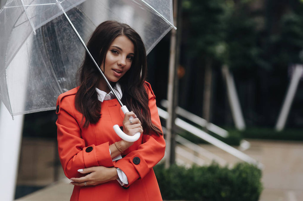 Woman portrait of young serious pretty girl posing at the city. Portrait of young woman in coat holding umbrella and looking at camera - Fotografie, Obrázek