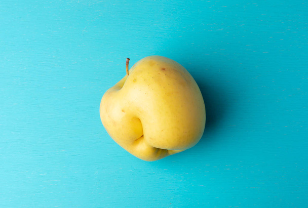 One ugly yellow apple on turquoise painted wooden background.  - Fotó, kép