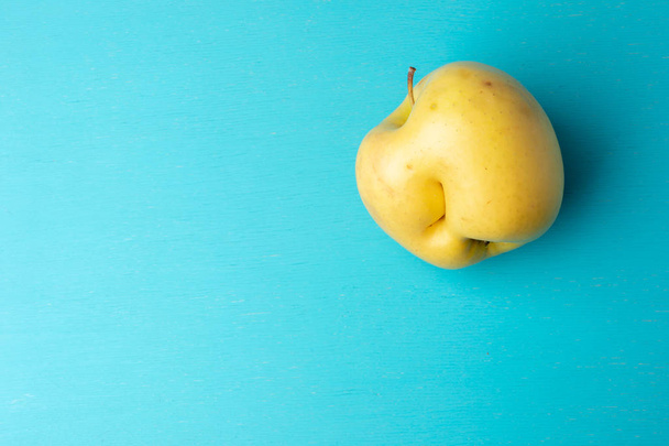 One ugly yellow apple with dent on turquoise background. - Valokuva, kuva