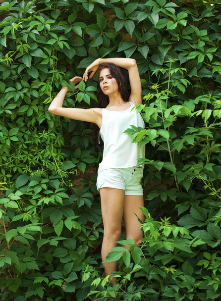 Beautiful brunette in a turquoise blouse posing against a green  - Photo, Image